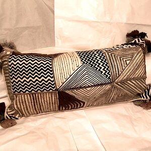 Decorative throw pillow. Embellished with geometric trims and tassels. 18”x 9”.